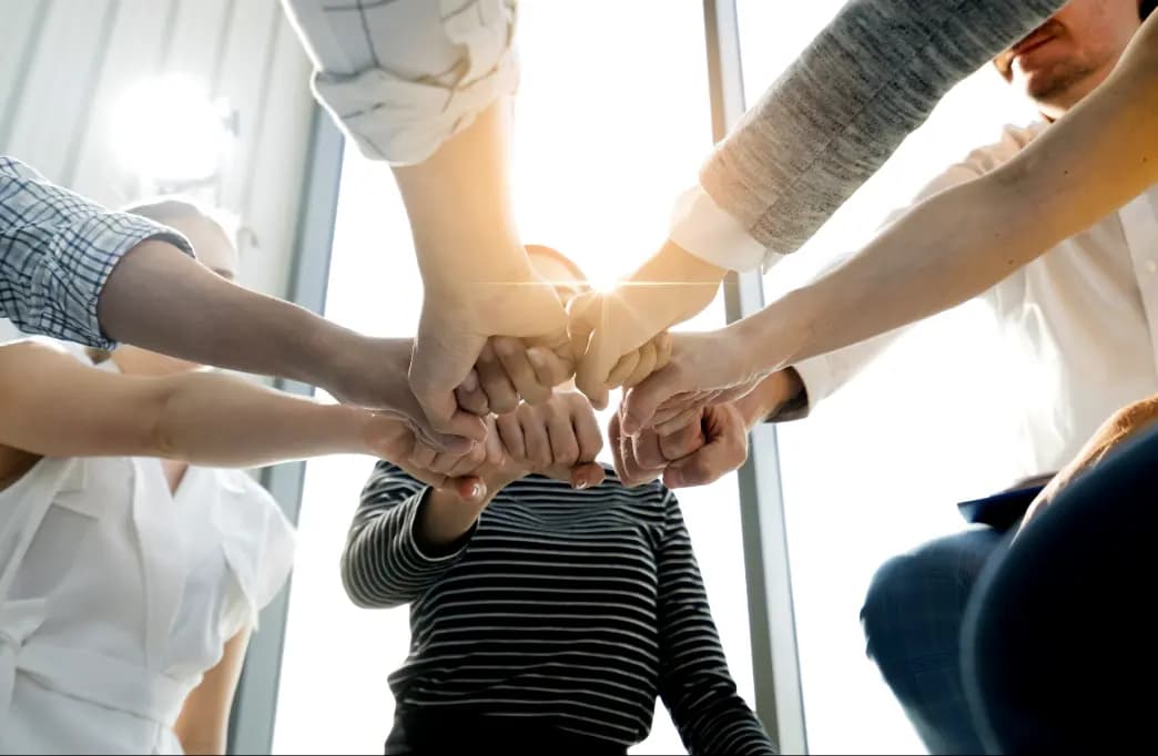Zespół pracowników stojących w kręgu i łączących dłonie w geście współpracy oraz jedności.
