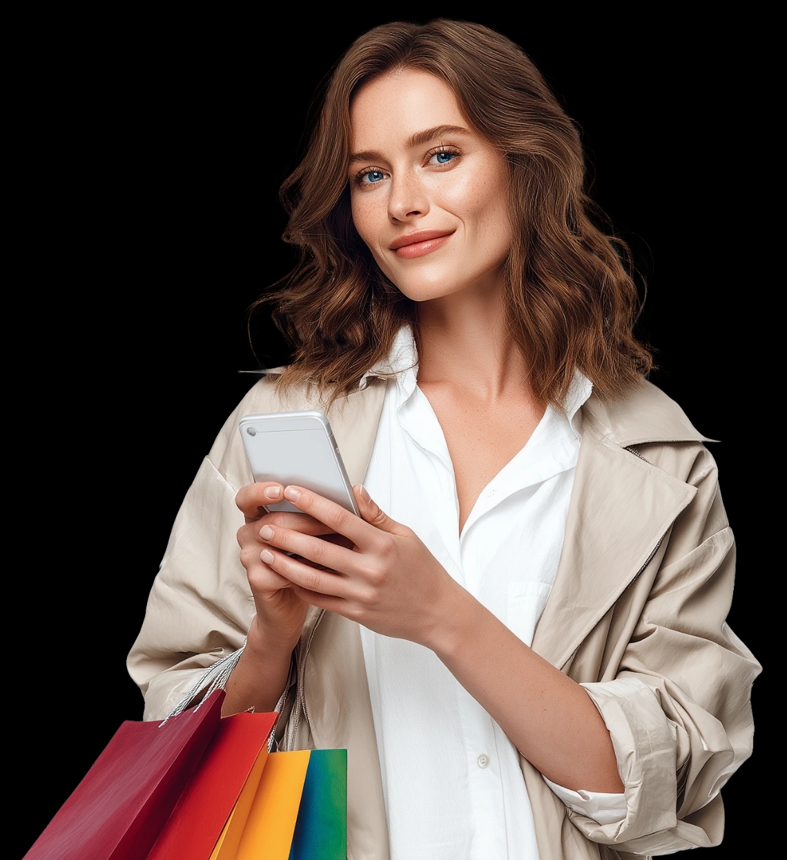 Młoda kobieta trzymająca smartfon i kolorowe torby zakupowe, ubrana w jasną koszulę i beżowy płaszcz.