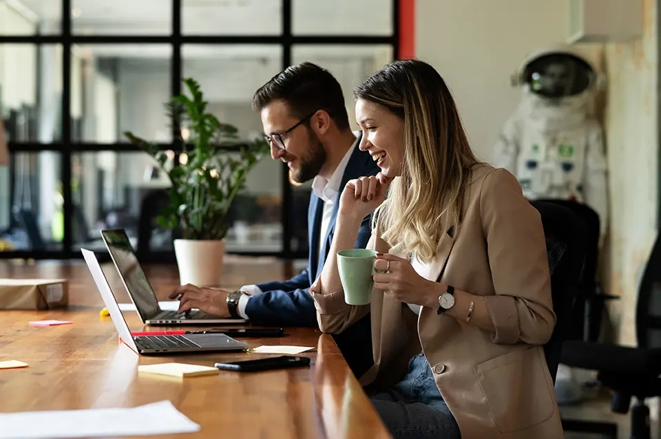 Dwoje pracowników biurowych pracuje przy laptopach w nowoczesnym biurze, współpraca i networking w przestrzeni coworkingowej