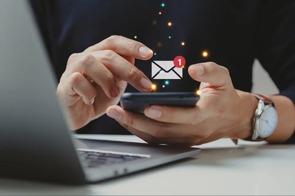 Mężczyzna pracujący przy laptopu sprawdza e-mail na komórce